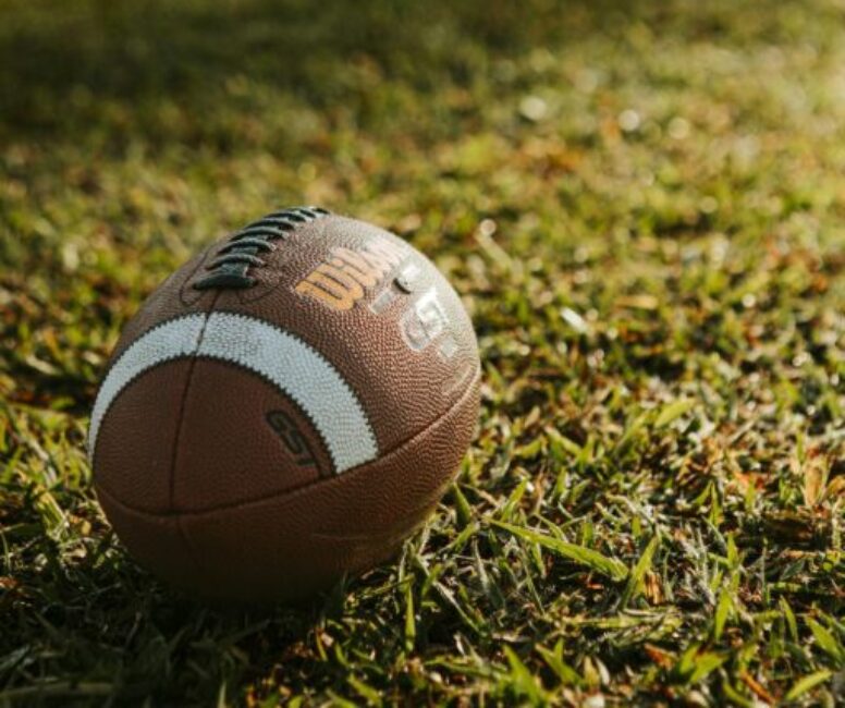 Close-up shot of a football resting on a sunlit grass field, ideal for sports themes.